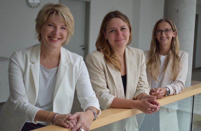 Die drei MMC Koordinatorinne lehnen im 1. OG über der Brüstung und lächeln in die Kamera. Von links nach rechts: Silke Hinze, Eva Tymko und Anika Weiß.